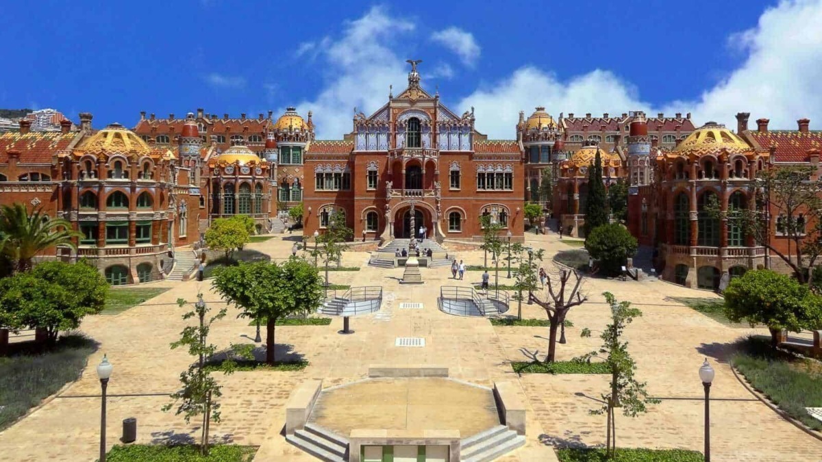 Castello in stile modernista, edificio storico affascinante con dettagli architettonici elaborati, situato in un parco verde con alberi e sentieri, sotto un cielo azzurro raggiante.