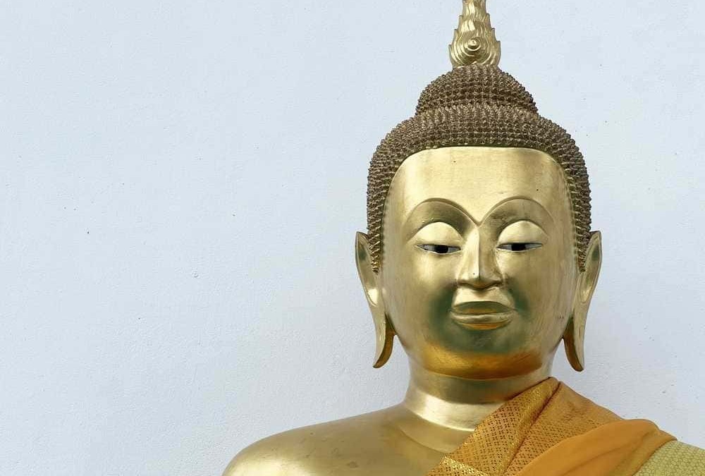 Buddha dorato con abiti tradizionali, statua sacra e simbolo di spiritualità e pace, su sfondo bianco, rappresentando serene pratiche di meditazione e filosofia buddista.