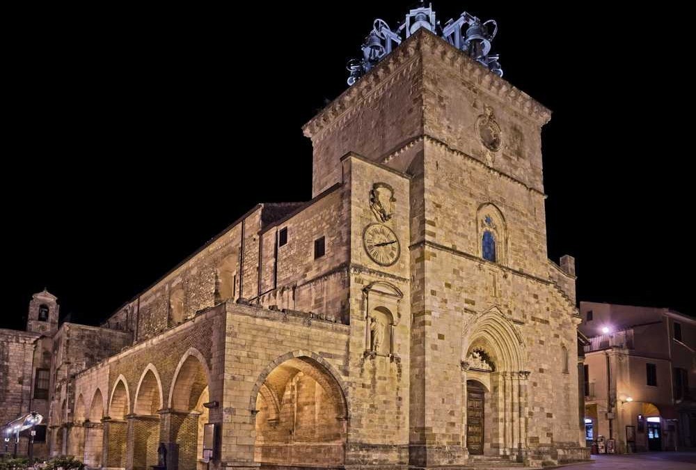 Vecchia chiesa in pietra con torre e orologio, illuminata di notte, stile architettonico storico, edificio religioso nel centro cittadino.