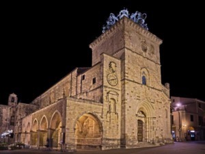 Vecchia chiesa in pietra con torre e orologio, illuminata di notte, stile architettonico storico, edificio religioso nel centro cittadino.