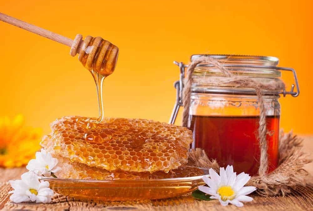 Miele di api con favo di miele naturale su tavola rustica, barattolo di miele fresco, fiori di camomilla bianchi sullo sfondo arancione caldo.
