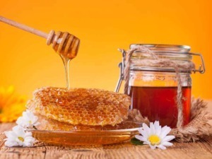 Miele di api con favo di miele naturale su tavola rustica, barattolo di miele fresco, fiori di camomilla bianchi sullo sfondo arancione caldo.