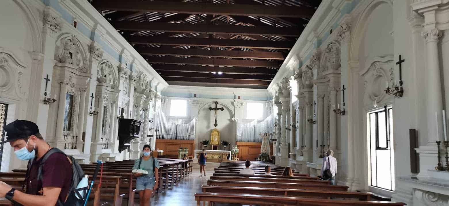 Immagine di una chiesa storica con pareti ornate, altare centrale e persone con mascherina. Interno di un luogo di culto con architettura barocca, atmosfera di spiritualità e arte religiosa, visitatori che esplorano lo spazio sacro.