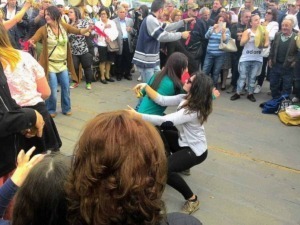 Punti di incontro e socializzazione di gruppi di amici in una piazza pubblica italiana, con persone che ballano e si divertono all'aperto, atmosfera festosa e vivace.