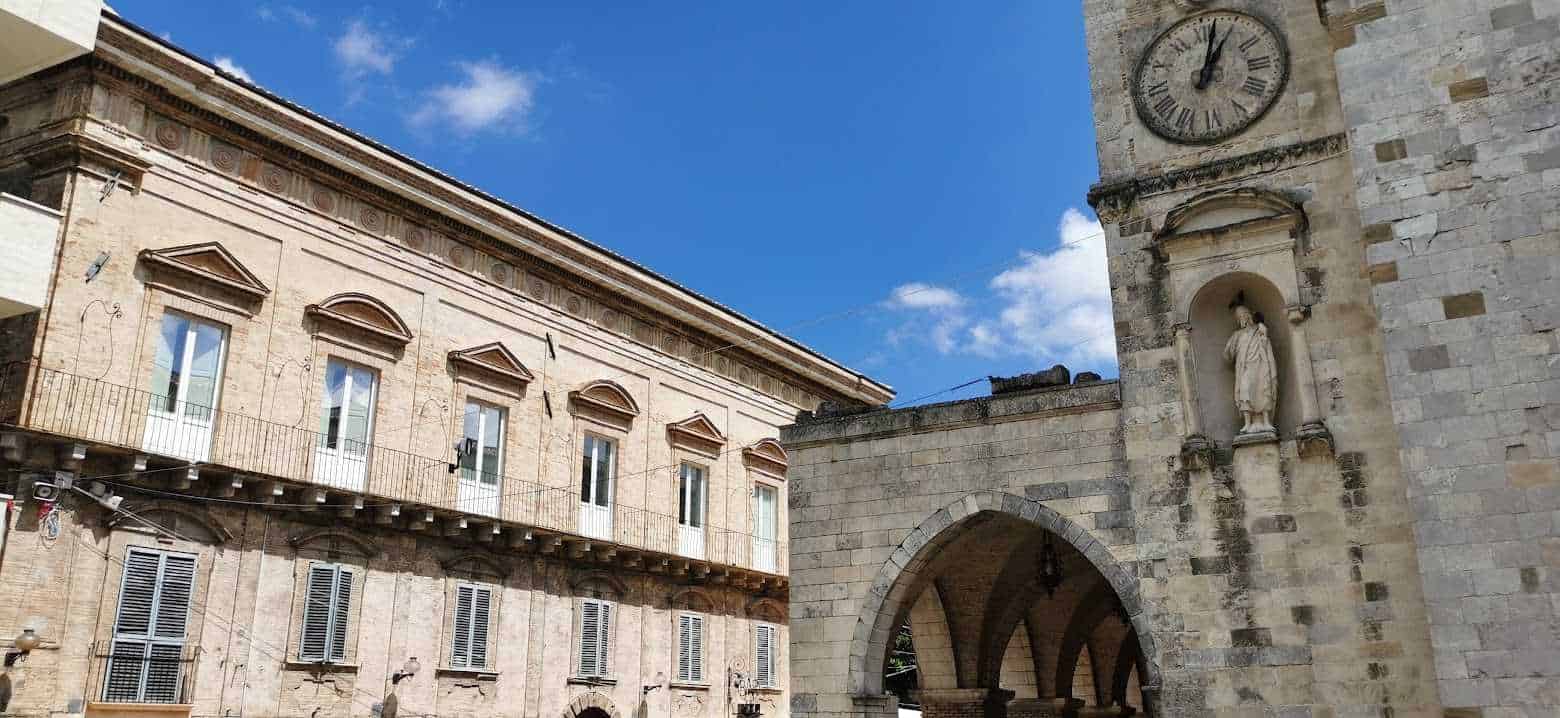 Vecchio edificio storico con archi e orologio sulla torre in pietra, documentazione architettonica e culturale con affreschi e decorazioni rinascimentali, situato in Italia, esempio di architettura storica.