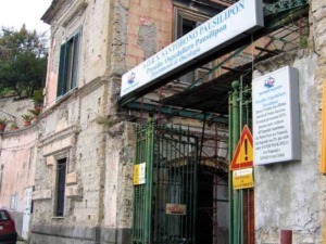 Vecchio edificio in pietra con segni di decadimento e segnaletica sanitaria, ingresso di un ospedale in Italia, struttura storica e in parte abbandonata.