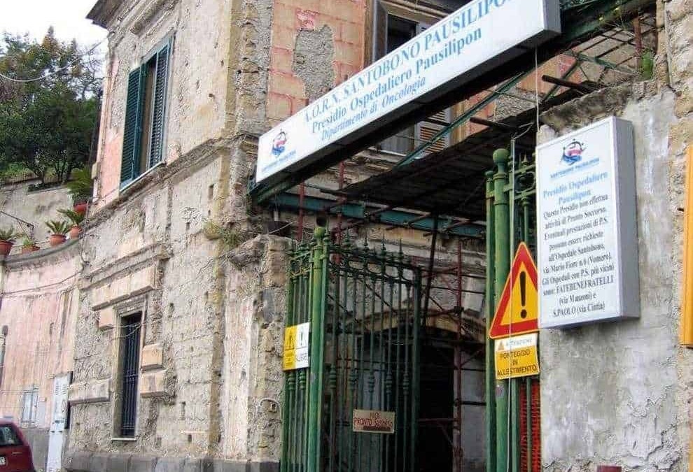 Vecchio edificio in pietra con segni di decadimento e segnaletica sanitaria, ingresso di un ospedale in Italia, struttura storica e in parte abbandonata.