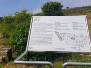 Cláudio di un pannello informativo all'aperto su antica archeologia e tradizioni della regione Paestum e Velia, situato in un'area naturale con colline e rovine storiche sullo sfondo.