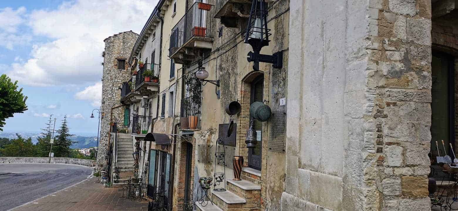 Vecchio edificio in pietra con oggetti d'epoca e piante sui balconi, stradina di paese in stile rustico, atmosfera suggestiva, presenza di lampioni e decorazioni vintage, esempio di architettura tradizionale italiana.