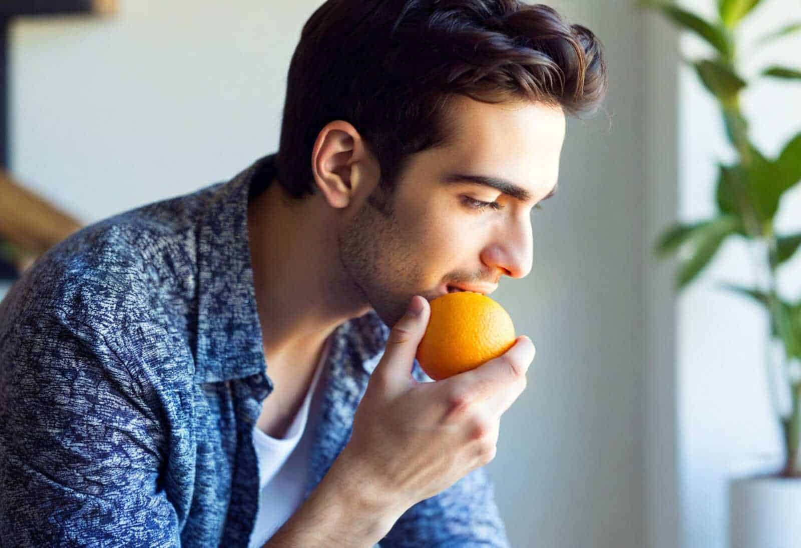 Arancia fresca mangiata da un giovane uomo, concetto di alimentazione sana e frutta naturale.