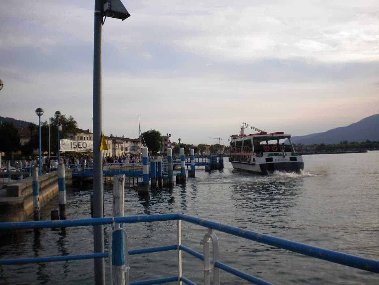 Cosa Vedere a Iseo città sul Lago di Iseo: centro storico, castello e lungolago 7 Porto turistico di Iseo con barca che si imbarca sul lago, atmosfera serale e paesaggio montano sullo sfondo, ideale per immagini di viaggi e viaggi in barca.