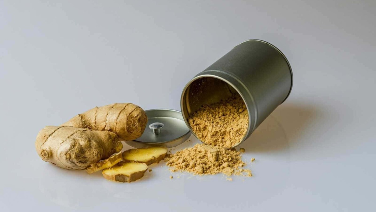 Polvere di zenzero in scatola con radici fresche di zenzero e alcune fette di zenzero fresco disposte su uno sfondo chiaro.