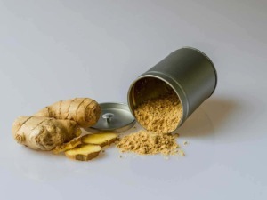 Polvere di zenzero in scatola con radici fresche di zenzero e alcune fette di zenzero fresco disposte su uno sfondo chiaro.