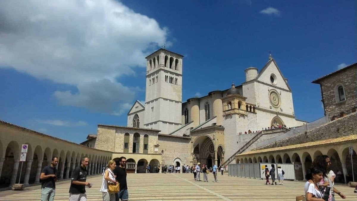 Antica basilica con piazza affollata e cielo blu, visite turistiche e architettura storica, Basilica di San Francesco Assisi, in Umbria, Italia.