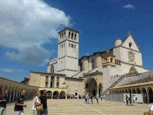 Antica basilica con piazza affollata e cielo blu, visite turistiche e architettura storica, Basilica di San Francesco Assisi, in Umbria, Italia.