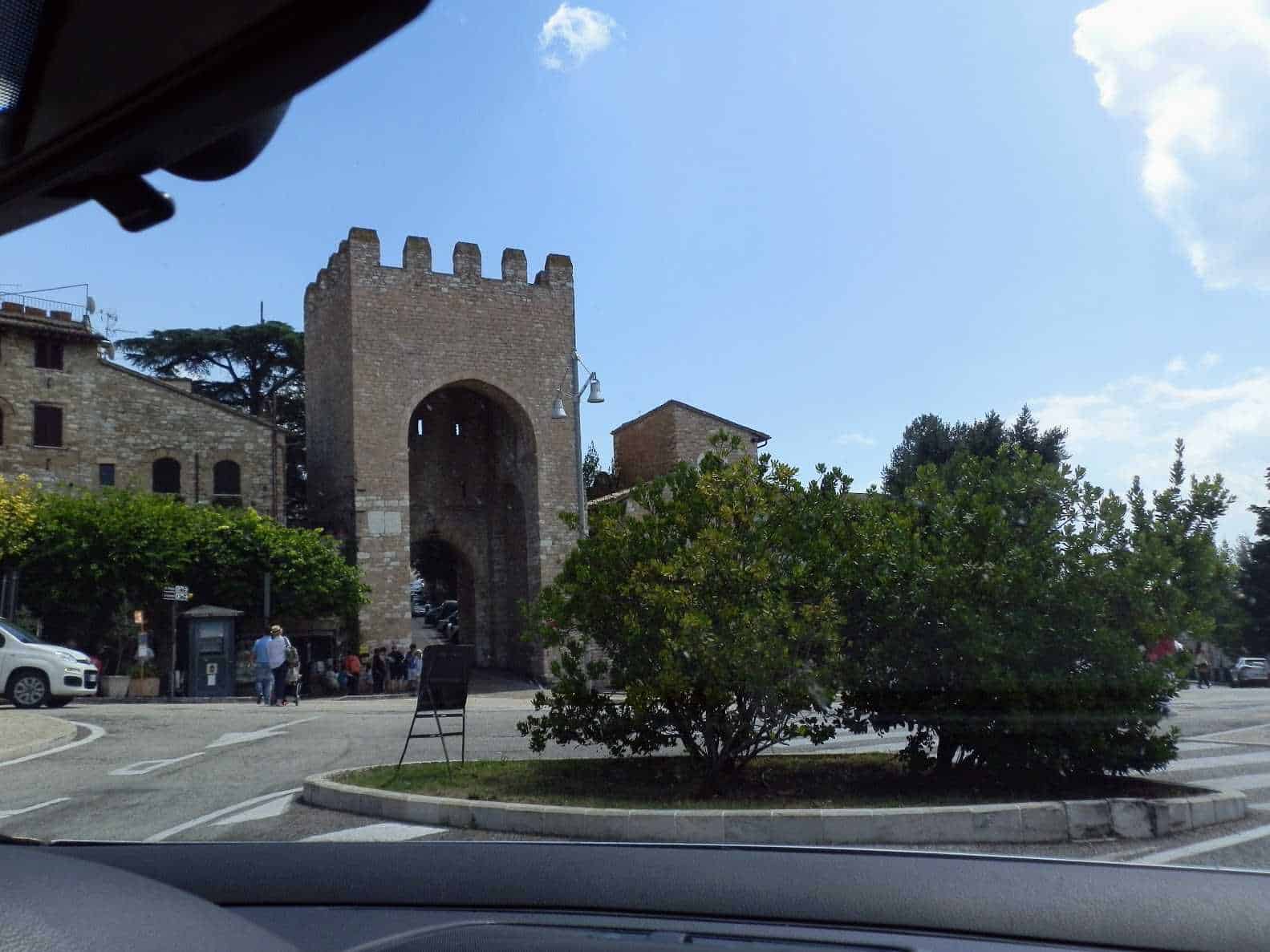 Antico arco Medievale in pietra situato nel centro storico di Assisi, un paese italiano, con persone che passeggiano e auto parcheggiate