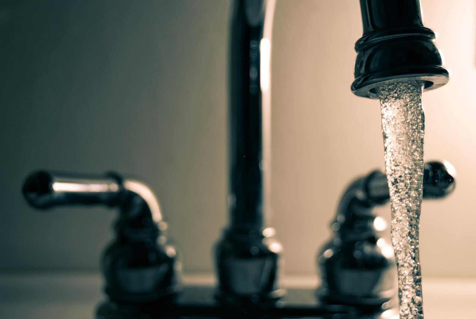 Rubinetto dell'acqua aperto con gocciolamento, dettaglio di un lavabo domestico, immagine simbolo di FAQ, problemi idraulici e manutenzione domestica.
