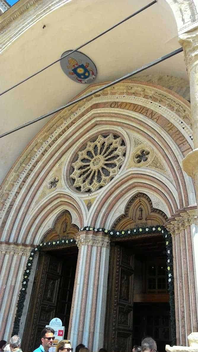 Ingresso della facciata della Basilica di San Francesco ad Assisi con dettagli architettonici in stile gotico, archi decorativi e rose in pietra.