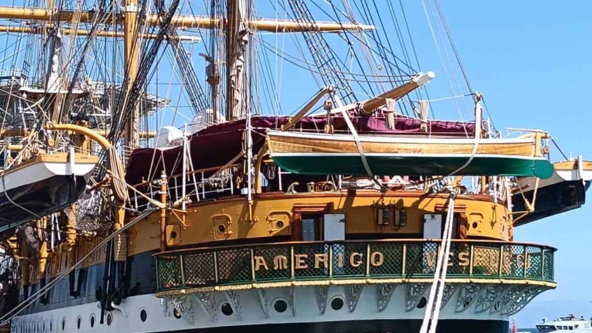 Antico veliero con vele spiegate ormeggiato al porto, bandiera italiana visibile, imbarcazione storica e di pregio, cielo azzurro e acqua blu sullo sfondo.