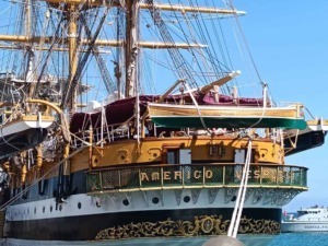 Antico veliero con vele spiegate ormeggiato al porto, bandiera italiana visibile, imbarcazione storica e di pregio, cielo azzurro e acqua blu sullo sfondo.
