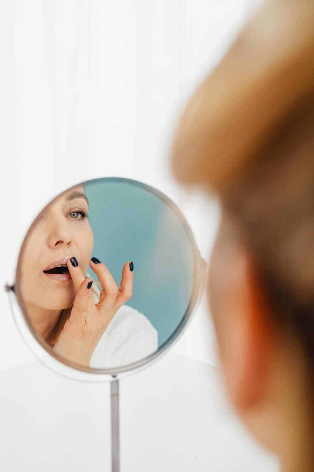 Specchio da tavolo con donna che si guarda e si sistema le labbra, dettaglio di bellezza e cura personale, ritratto in primo piano, ispirazione per beauty e cosmetici, immagini di auto-cura.