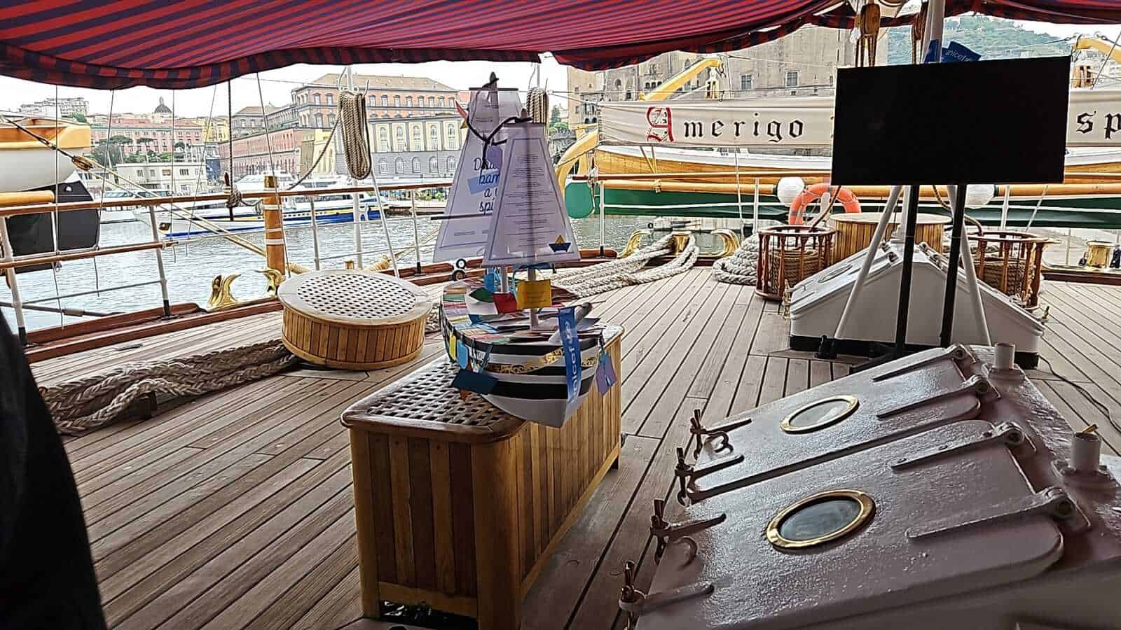 Amerigo Vespucci a Napoli 2025: cosa sapere 5 Sedia e arredamento su una barca a vela con vista sul porto e sulle barche circostanti.