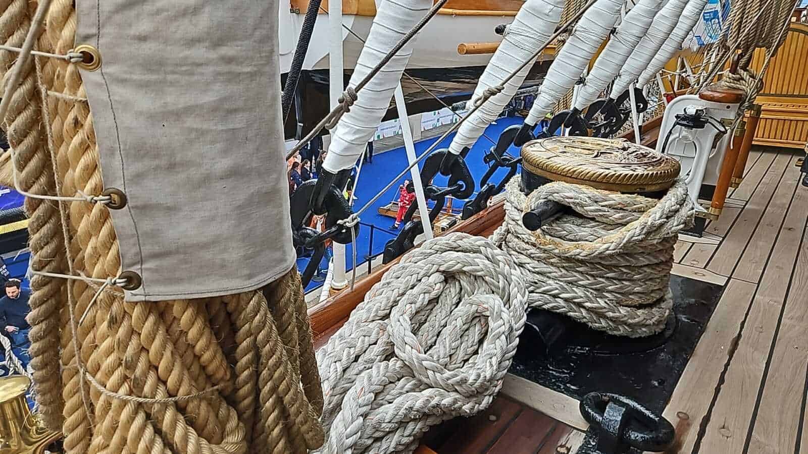 Amerigo Vespucci a Napoli 2025: cosa sapere 10 Corda di varo e ganci di ormeggio su una barca a vela, dettagli su attrezzature nautiche e setup marittimo, materiali robusti e stile nautico vicino al ponte di legno.