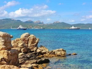 Baia con yacht di lusso e montagne sullo sfondo, riviera mediterranea, mare cristallino, coste rocciose, vacanze estive in Italia, paesaggi marini, turismo di lusso.