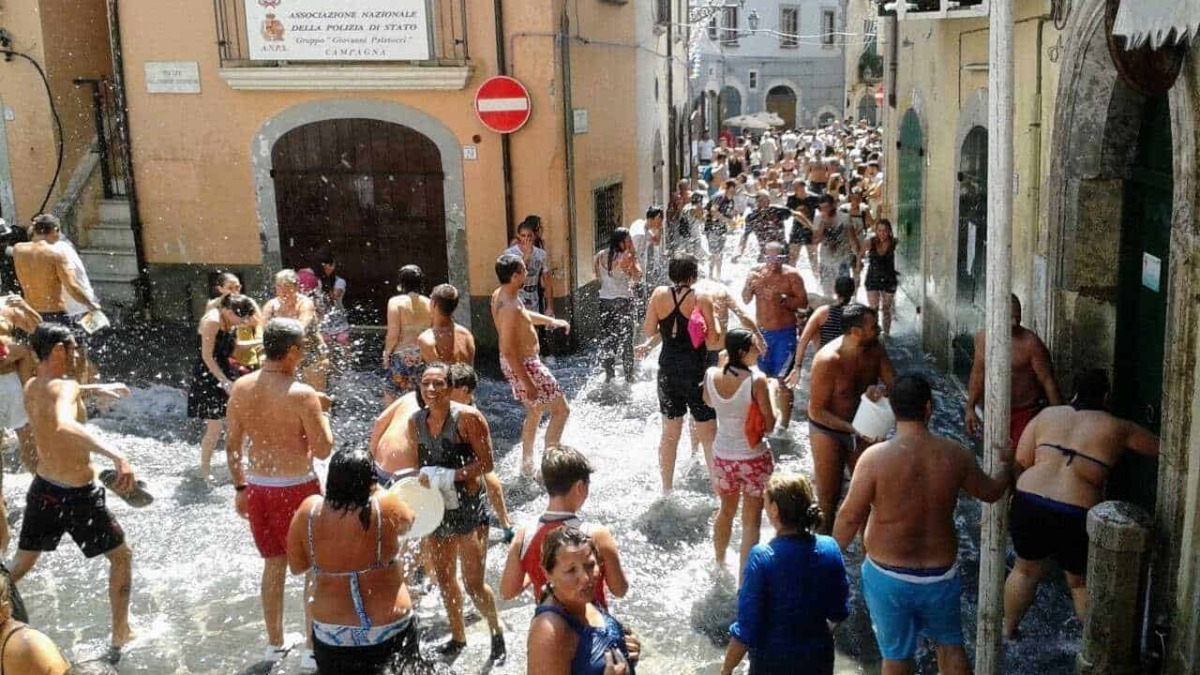 Bagno in strade affollate di persone che si rinfrescano in una calda giornata estiva in un centro storico italiano. Sfondo di edifici colorati e architettura tradizionale.
