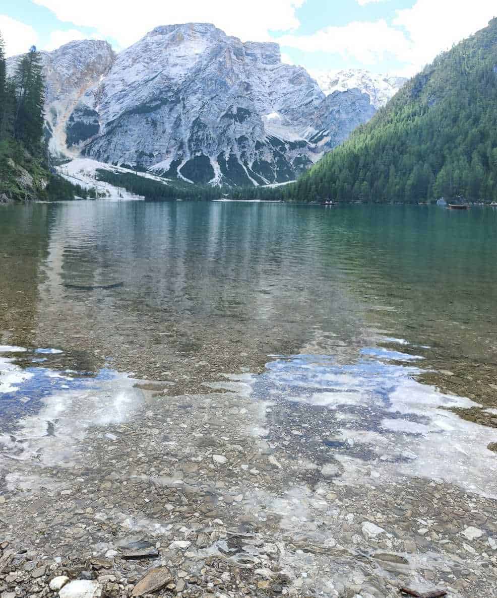 Montagne innevate e lago cristallino con sponde rocciose, paesaggio naturale di grande bellezza in Dolomiti, Italia, perfetto per appassionati di escursionismo e fotografia.