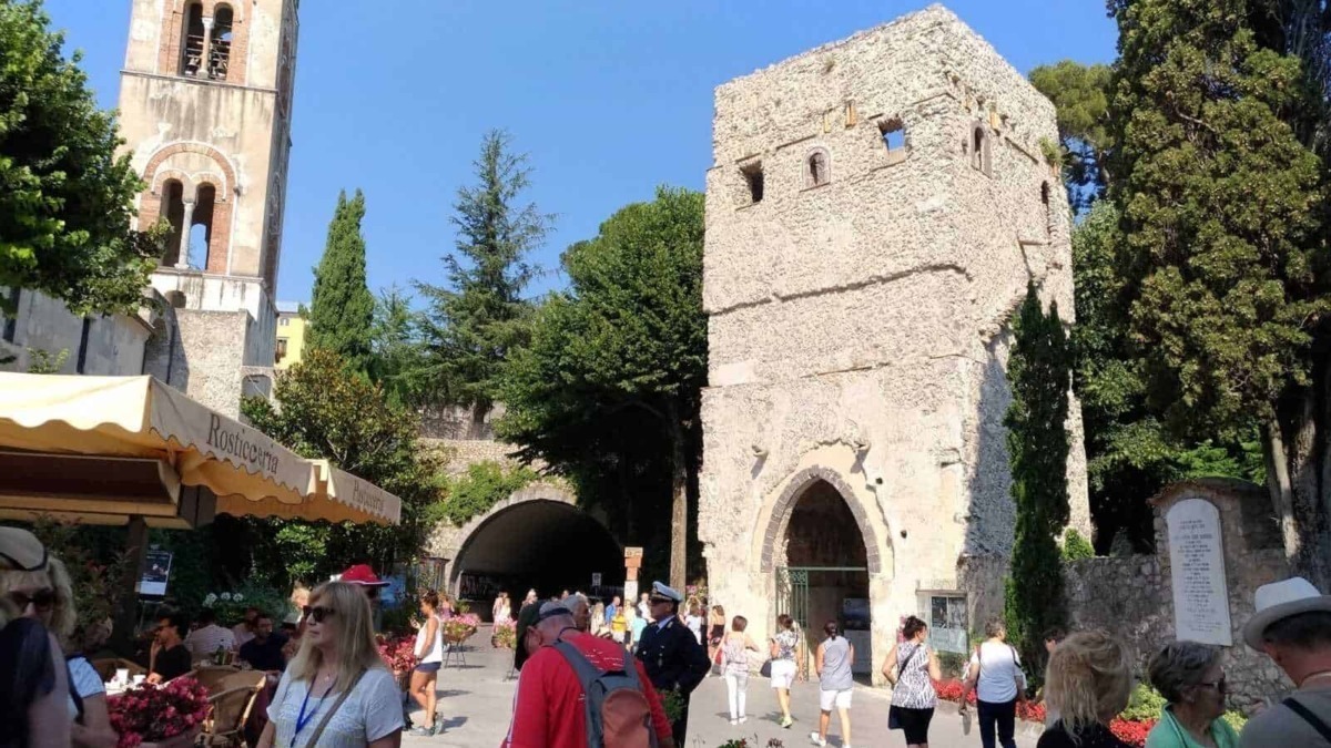 Antico torre e chiesa storica a Ravello con turisti e sfondo cielo blu, famosa attrazione culturale e storica in Italia.