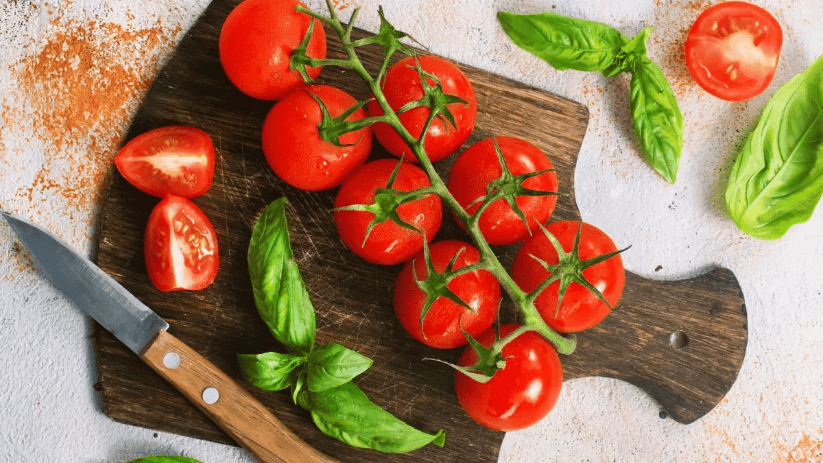 Pomodori ciliegini freschi e maturi con basilico su tagliere di legno, ideale per ricette mediterranee e insalate salutari.