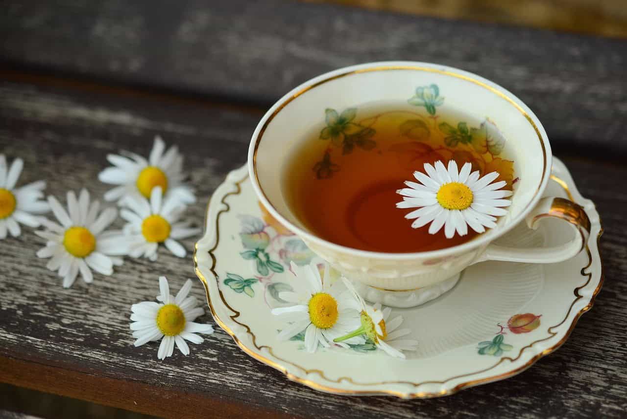 Tisana a base di camomilla in tazza di porcellana decorata con fiori, sul tavolo di legno.