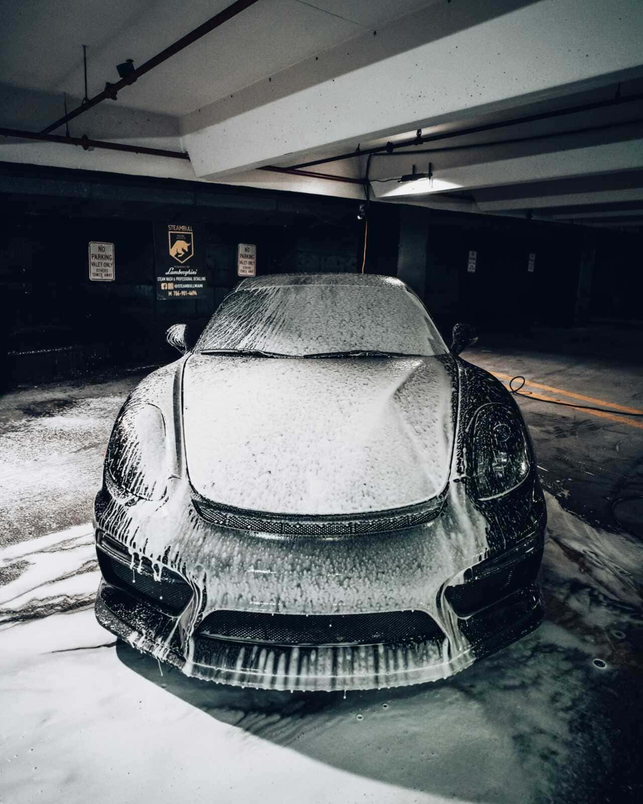 Pulizia auto Lamborghini con schiuma nel parcheggio sotterraneo, cura e manutenzione del veicolo di lusso, dettagli estetici e servizio professionale.