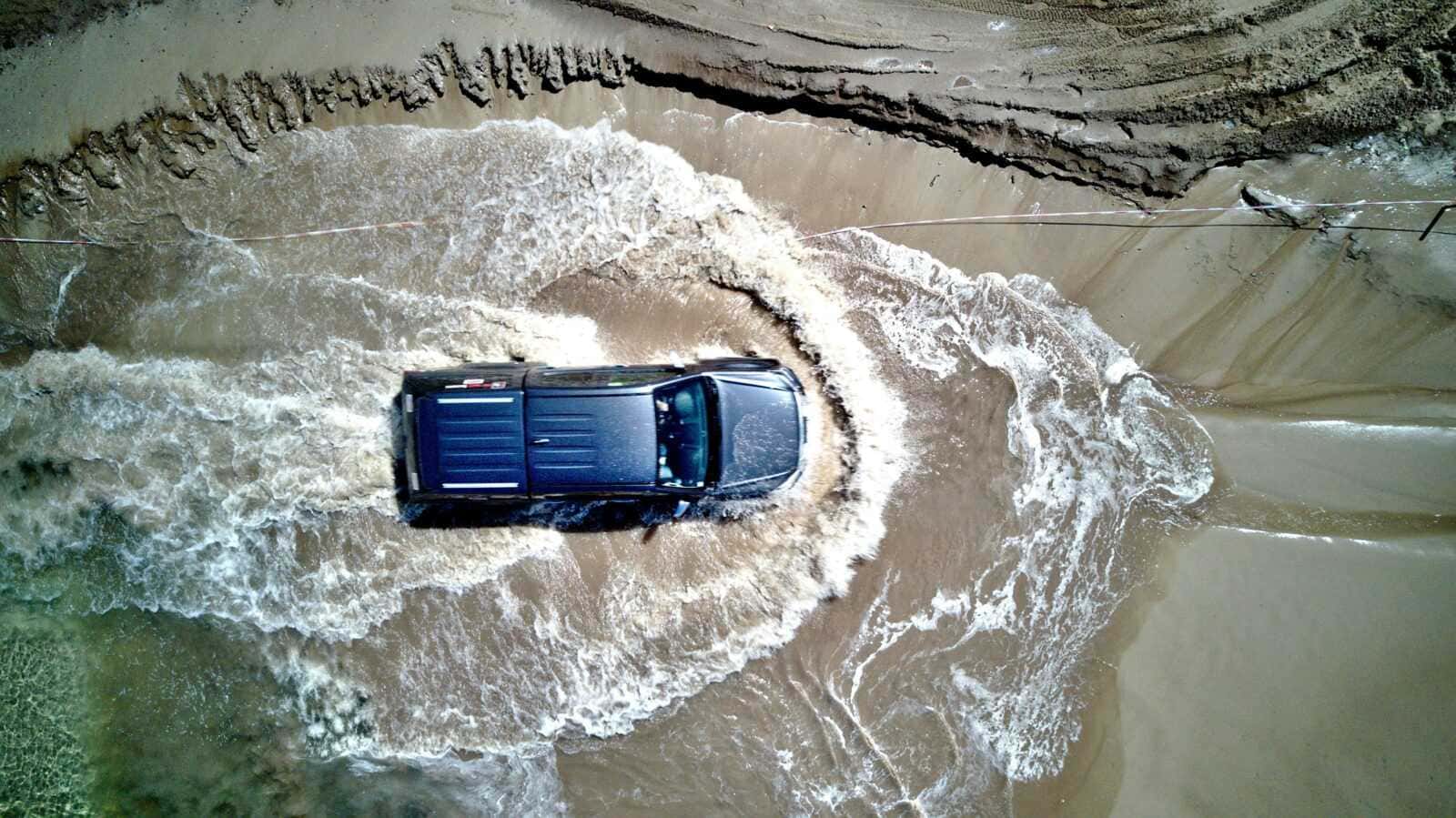 Auto 4x4 che attraversa un'enorme pozzanghera di fango e acqua, sfiorando le pareti di un canyon naturale, in un'avventura off-road in un paesaggio selvaggio e accidentato.