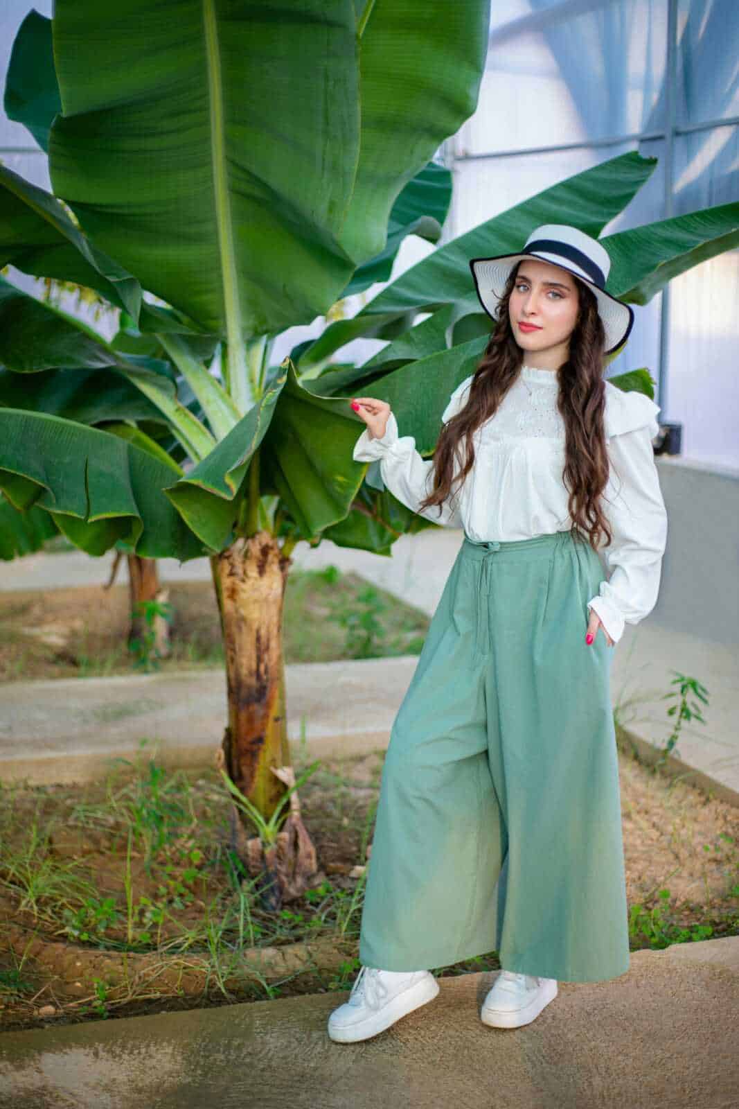 Banana plant nell'ambiente di una serra, donna giovane con cappello e abiti alla moda, moda sostenibile, giardinaggio urbano, verde lussureggiante, stile casual elegante, moda eco-friendly, accessori di moda legge, oggetti di moda e natura.