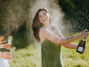 Festa all'aperto con donna felice che spruzza spumante durante un brindisi tra amici in un giardino soleggiato.