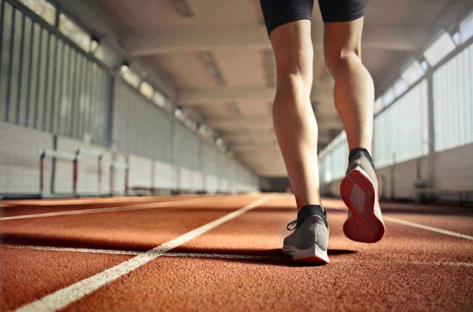 Scarpe da corsa e muscoli delle gambe di un atleta in allenamento su una pista indoor colorata.