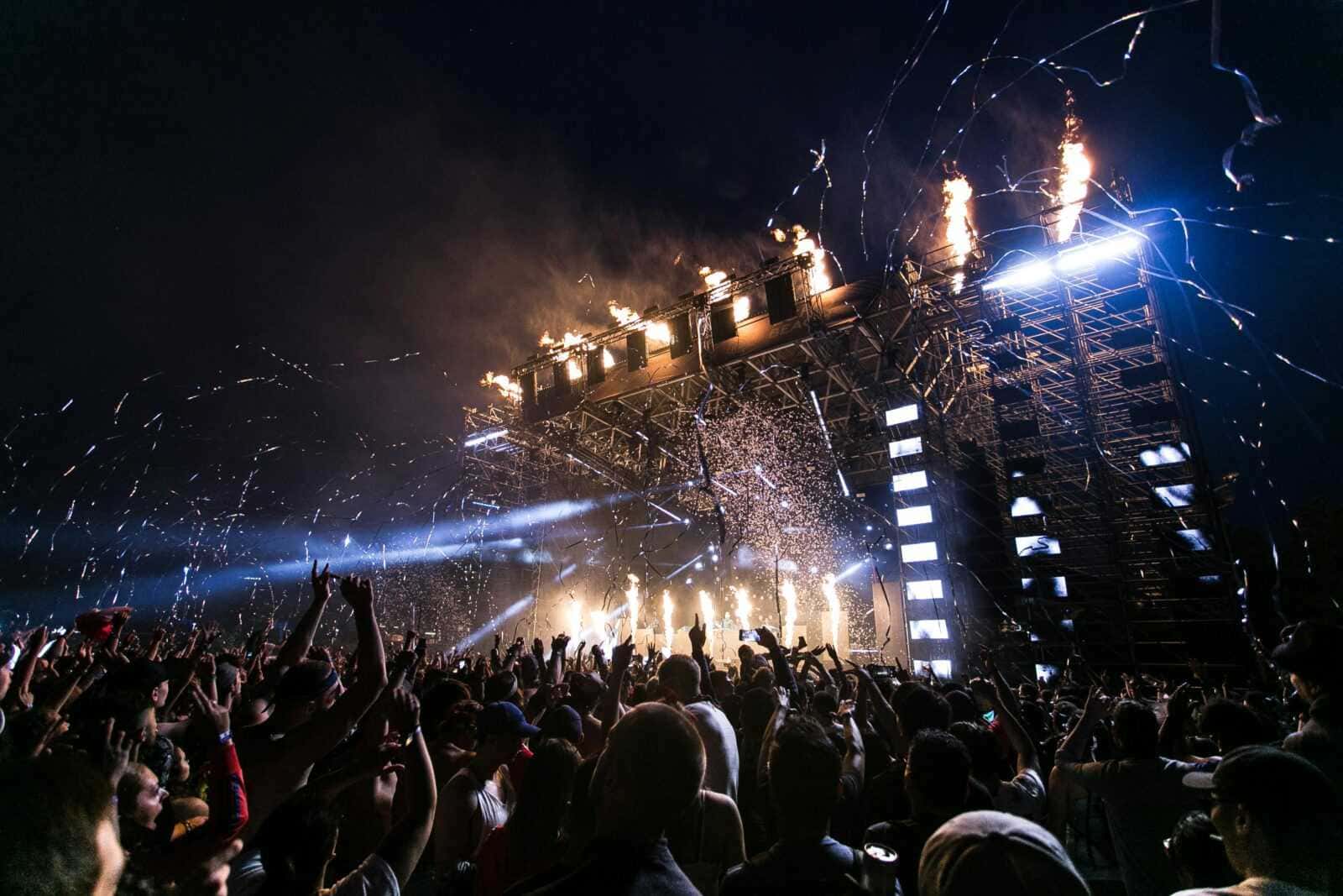 Festa di musica dal vivo con fuochi d'artificio, luci e pubblico entusiasta che si diverte a un concerto notturno, atmosfera di festa e emozione vibrante.