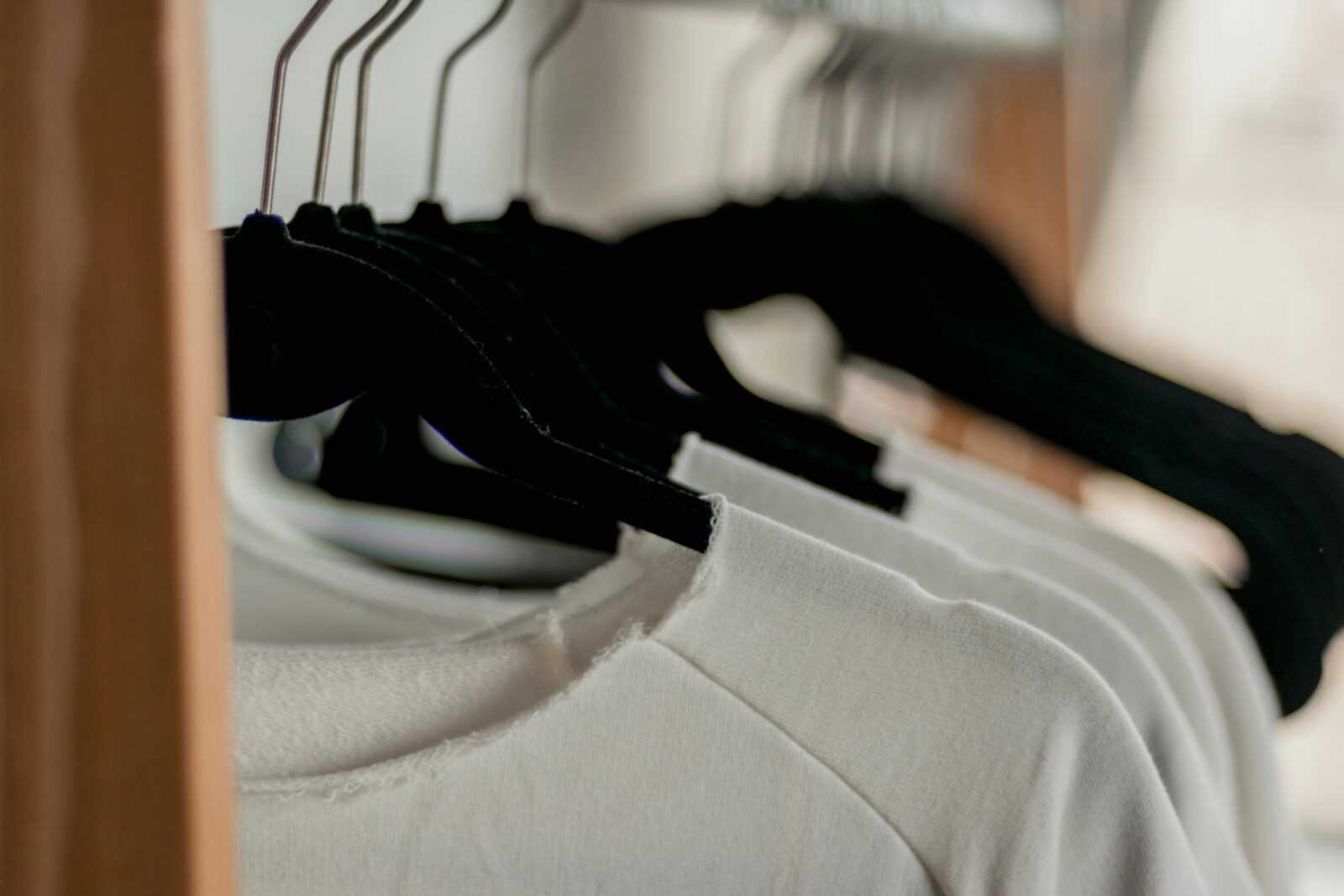 Vestiti su appendiabiti nel guardaroba, abbigliamento casual, magliette e felpe in bianco e nero, organizzazione wardrobe, stile minimalista.
