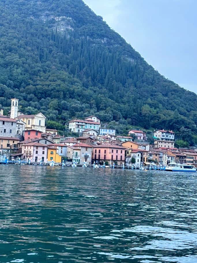 Colorato paesino sul lago con case color pastello e montagne verdi sullo sfondo, ideale per un’articolo su destinazioni di viaggio e bellezze naturali italiane.