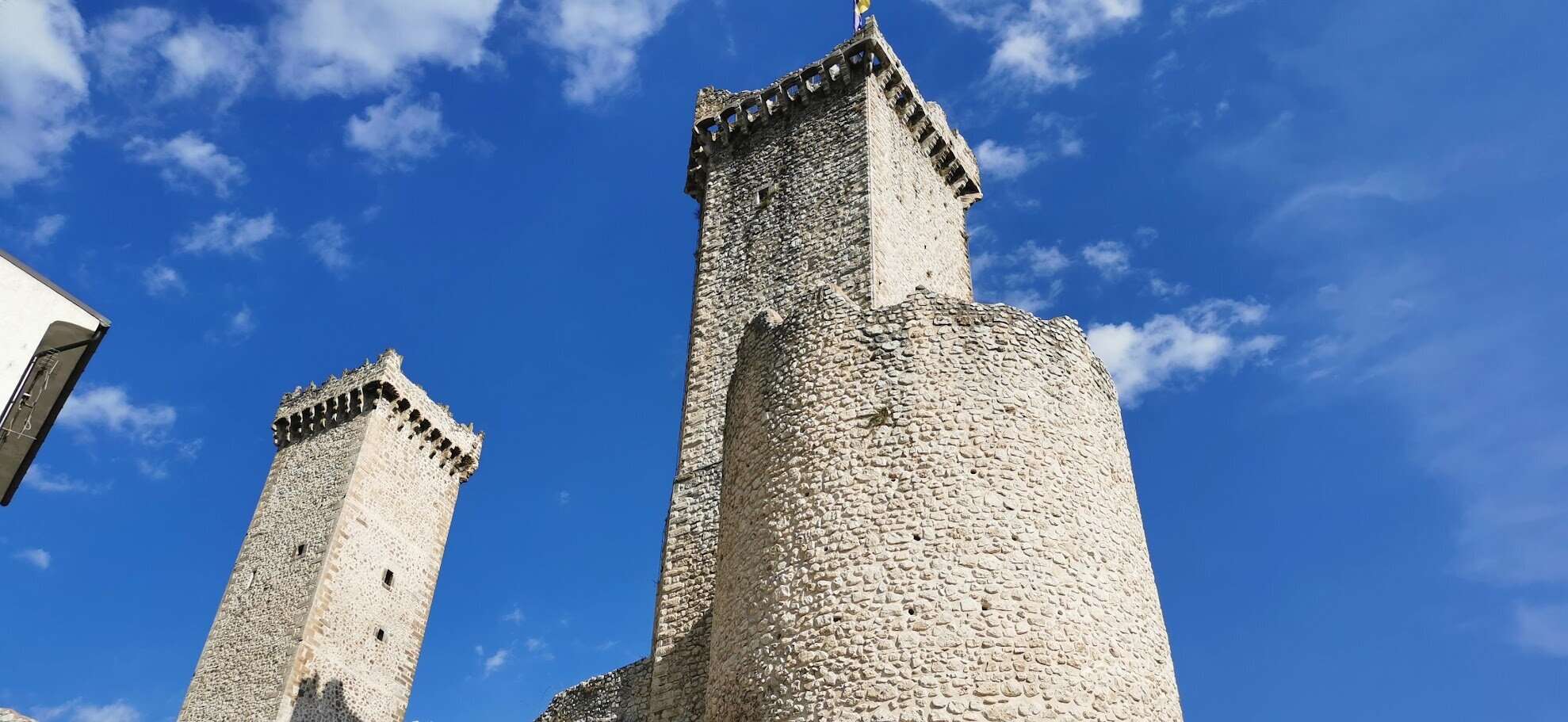 Torri medievali in pietra in un paesaggio urbano italiano, simbolo di storia e architettura antica, con cielo azzurro e nuvole bianche sullo sfondo.