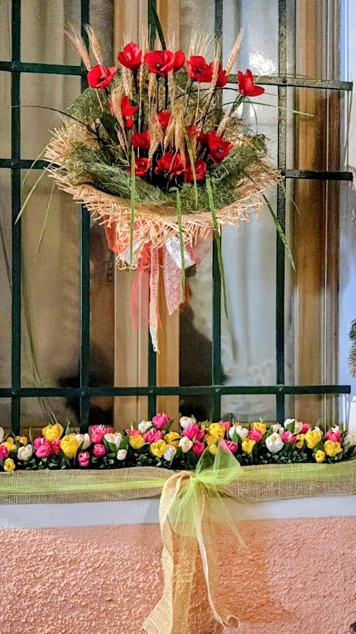 Fiori rossi e gialli decorativi con nastri colorati per occasioni speciali, ornati su una ringhiera con decorazioni floreali e nastri di tessuto, creando un elegante ambiente festivo.
