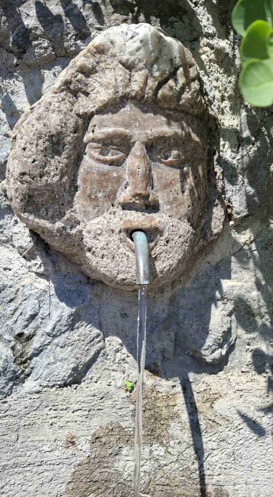 Perché visitare la Torre dello Ziro? 8 Vecchio fontanile decorativo in pietra con testa umana scolpita e tubatura in ferro che eroga acqua tra le rovine della della Torre dello Ziro