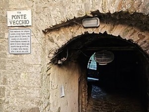 Ingresso di un passaggio storico in pietra con lampada, situato sotto un arco vicino a una strada antica, perfetto per esplorare il patrimonio culturale e architettonico italiano.