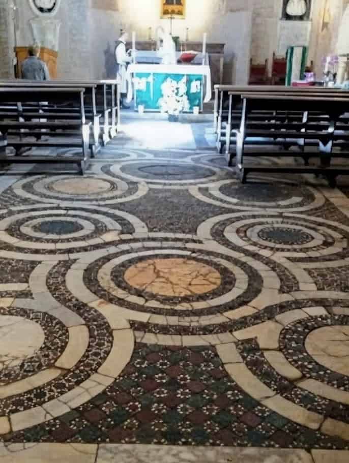 Croce di pietra ricca di dettagli artistici all'interno di una chiesa antica. Pavimento in marmo con motivi circolari e geometrie intricate, ideali per apprezzare l'arte sacra e l'architettura storica.