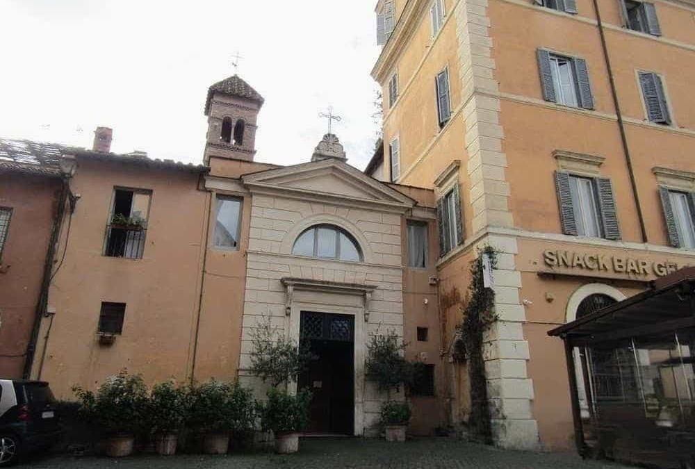 Vecchia chiesa nel centro di Roma, situata vicino a un edificio residenziale, con un piccolo cortile e piante, testimonianza di architettura storica italiana e ambientazione urbana.
