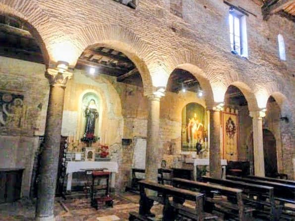  cappella laterale dedicata a San Benedetto e a Santa Scolastica. Antico interno di chiesa con archi in pietra e dipinti sacri, atmosfera suggestiva e tranquilla, ideale per spiritualità e riflessione religiosa.