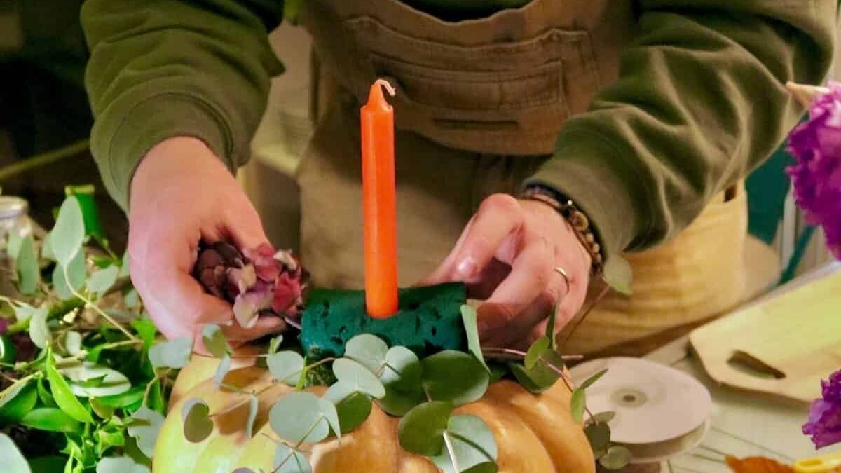 Ampio di una persona che crea una composizione artistica con zucche, foglie e fiori, utilizzando elementi naturali e decorativi per decorare uno spazio, con attenzione ai dettagli e alla creatività.
