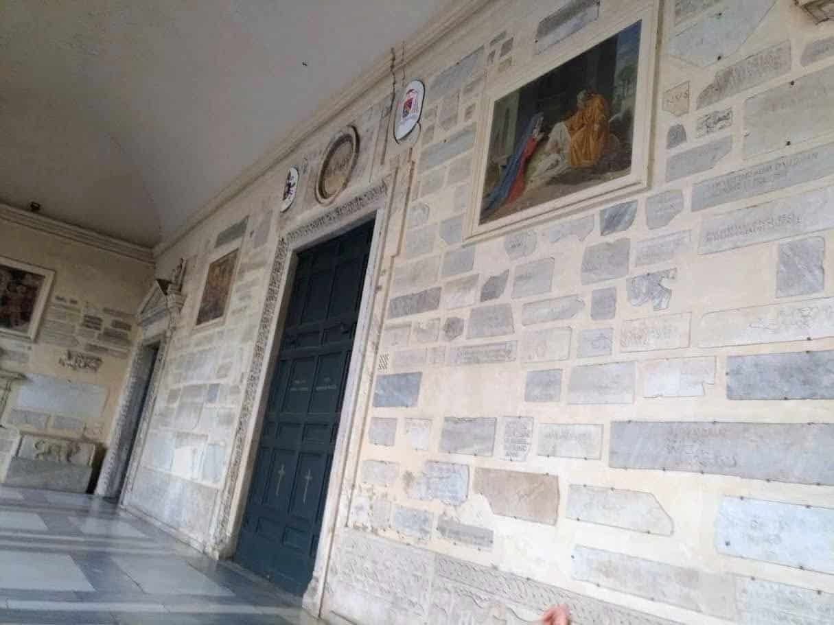 Portone su parete in pietra con dipinti e piatti decorativi, ambiente storico con dettagli artistici e architettonici, decorazioni murali di valore culturale e religioso, pareti in pietra con iscrizioni e affreschi, design degli interni di un edificio storico, dettagli artistici e religiosi in un contesto storico, decorazioni di pregio e arte sacra in un ambiente di culto italiano.